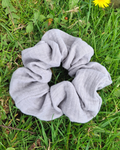 Grey scrunchie on green grass with a yellow flower in the background