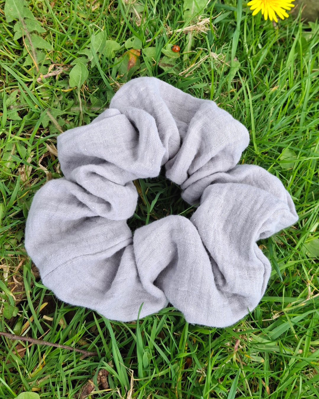 Grey scrunchie on green grass with a yellow flower in the background