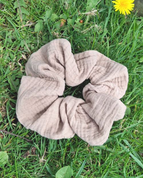 Beige scrunchie on grass with a dandelion in the background